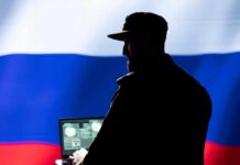Silhouette of a military personnel in front of the Russian flag using a laptop