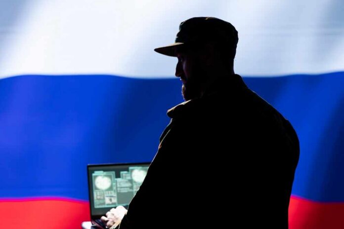 Silhouette of a military personnel in front of the Russian flag using a laptop