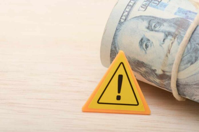 A roll of cash next to a warning sign on a wooden surface