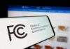 Close-up of a mobile device displaying the FCC logo with a website in the background