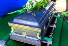 A silver casket adorned with flowers at a gravesite