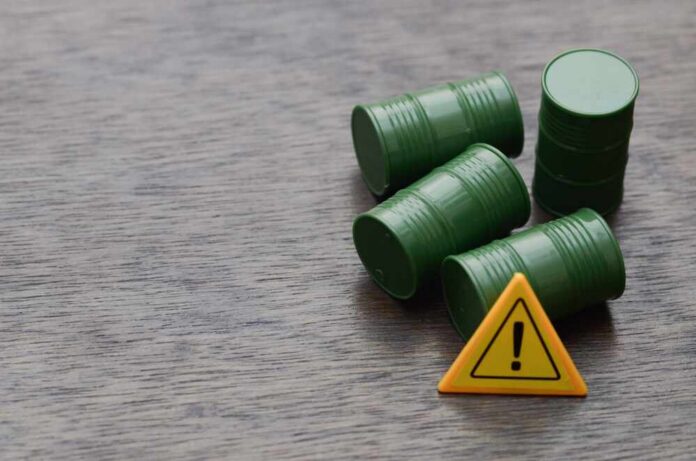 shutterstock_2663559179.jpg Four green barrels and a warning sign on a wooden surface