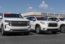 Two white SUVs parked at a used car dealership with price tags visible