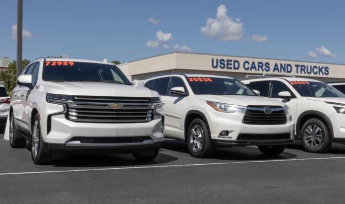 shutterstock_2671336851.jpg Two white SUVs parked at a used car dealership with price tags visible