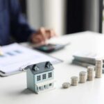 A miniature house model with stacks of coins and a person calculating finances