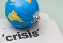 A small globe resting on a newspaper with the word 'crisis'