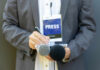 Journalist with press badge, notebook, and microphones.