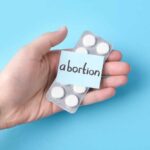 Hand holding a blister pack of white pills labeled 'abortion'