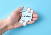 Hand holding a blister pack of white pills labeled 'abortion'