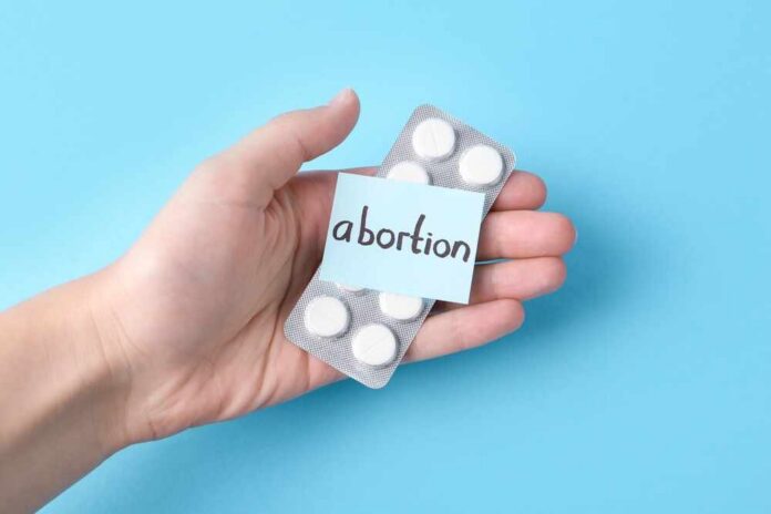 Hand holding a blister pack of white pills labeled 'abortion'