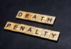 Wooden letter tiles spelling DEATH PENALTY on a dark background
