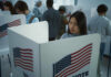 People voting in booths with American flags.