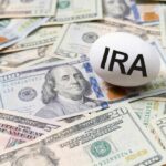 An egg labeled 'IRA' placed on a pile of U.S. dollar bills