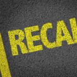 Robotaxis SWEPT Into Waterway — RECALLED Yellow 'RECALL' text on a dark asphalt surface