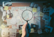 Magnifying glass over investigation board with photos and strings.