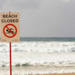 Sign indicating the beach is closed with a no swimming symbol
