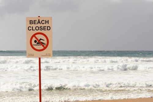 "beach,Closed",Sign,With,Choppy,Seas,In,The,Background,At Sign indicating the beach is closed with a no swimming symbol