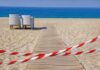 A wooden pathway leading to the beach with restricted access tape and chairs in the background