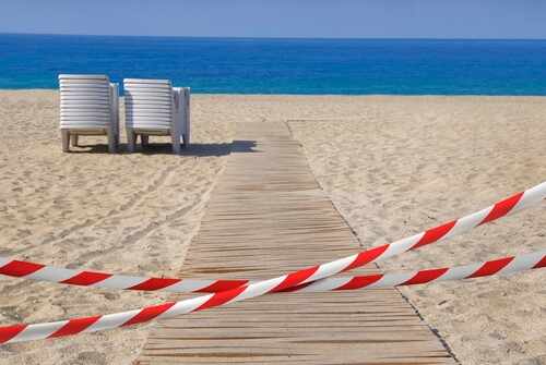 A wooden pathway leading to the beach with restricted access tape and chairs in the background