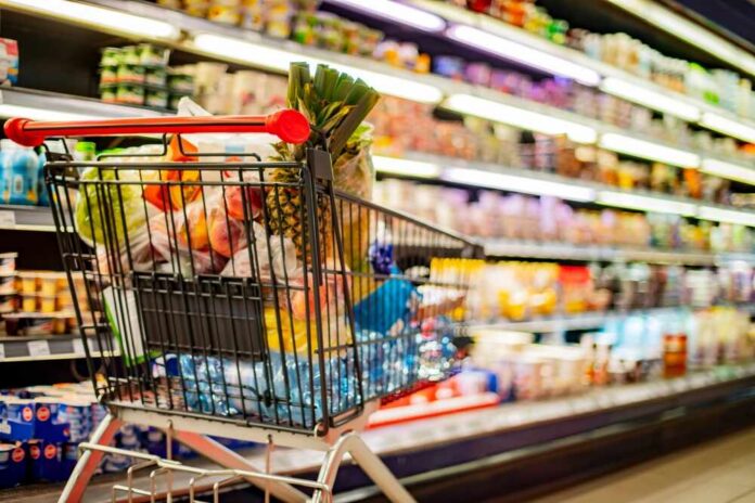 Shopping cart filled with various groceries in a supermarket aisle