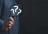 Hand holding magnifying glass with question marks.