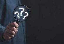 Hand holding magnifying glass with question marks.