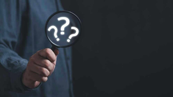 Hand holding magnifying glass with question marks.