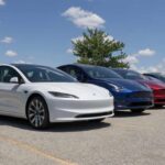 A lineup of Tesla electric vehicles parked outdoors under a blue sky