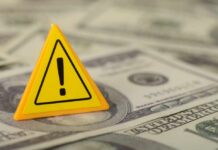 War Tax Hits Every Kitchen Table A yellow warning sign placed on a pile of dollar bills