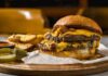 A double cheeseburger with melted cheese and pickles served with potato wedges