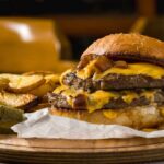 A double cheeseburger with melted cheese and pickles served with potato wedges