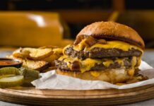 A double cheeseburger with melted cheese and pickles served with potato wedges
