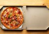 A pizza with various toppings in an open pizza box on a wooden table