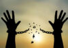 Silhouetted hands breaking chains against sunset sky.