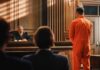 Defendant in orange jumpsuit stands before a judge in a courtroom
