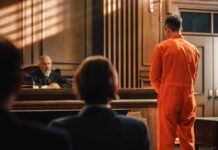 Defendant in orange jumpsuit stands before a judge in a courtroom