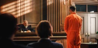 Defendant in orange jumpsuit stands before a judge in a courtroom