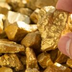 Hand holding a rough gold nugget among scattered gold pieces