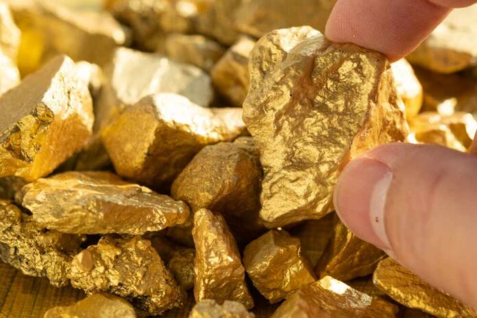 Hand holding a rough gold nugget among scattered gold pieces