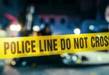 Deadly Festival Bloodbath Panics Crowd Police line caution tape at a crime scene with blurred figures in the background