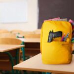 A yellow backpack with a gun partially visible in a classroom setting