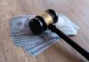 Judge Triggers Costly Trump Payout Judge’s gavel resting on a stack of US hundred-dollar bills
