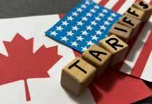 Smoke Tariff Gambit Shocks Ottawa Wooden blocks spelling 'TARIFFS' on flags of Canada and the USA