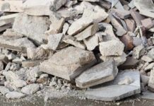 People examining rubble of collapsed building in sunlight.