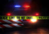 Police car with flashing lights behind caution tape.