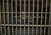 Empty, rusty barred jail cell with metal bunks.