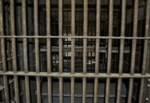 Empty, rusty barred jail cell with metal bunks.