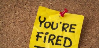 A yellow sticky note pinned to a corkboard with the words 'YOU'RE FIRED' written on it