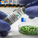 A laboratory technician holding a vial labeled 'Listeria monocytogenes' above a petri dish with green culture