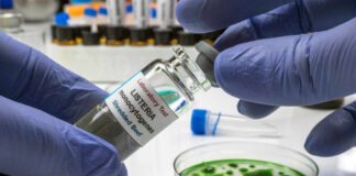 A laboratory technician holding a vial labeled 'Listeria monocytogenes' above a petri dish with green culture